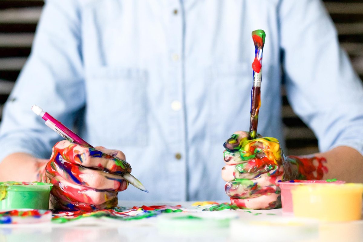 image of hands and paintbrushes covered in many colours of paint